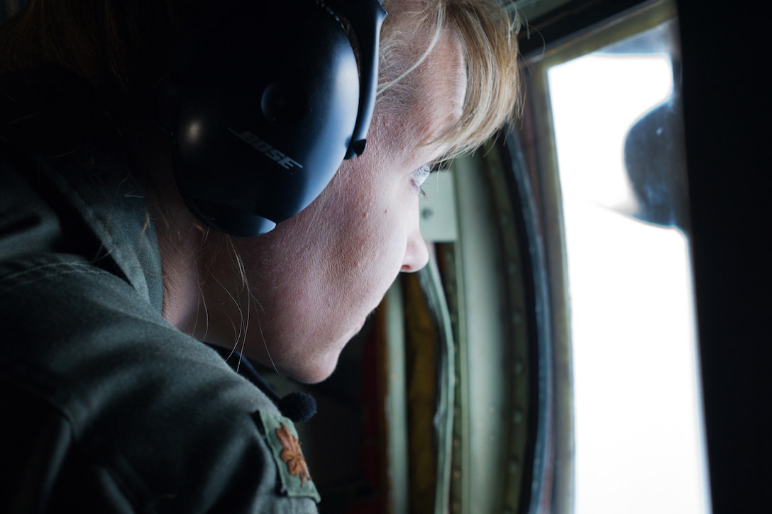 A member of the Air Force looks out a plane window.