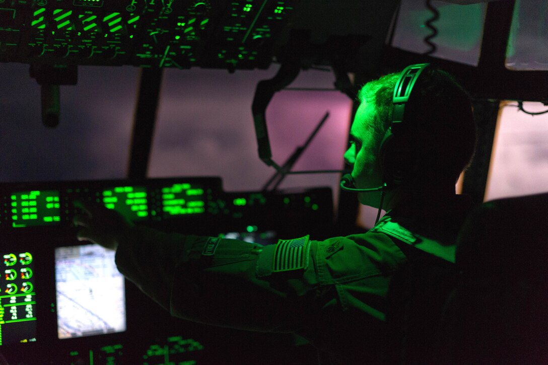 A member of the Air Force sits at the controls of an airplane with clouds visible though the windscreen.