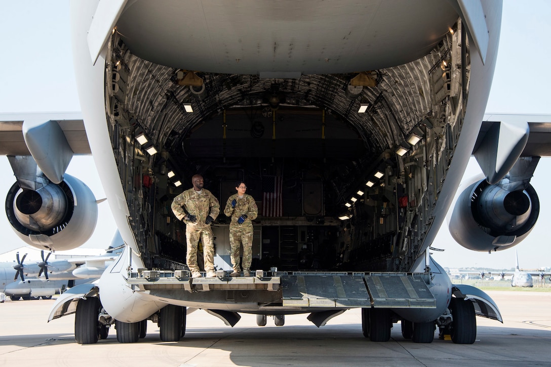 Two airmen stand in the back of a C-17 Globemaster III.