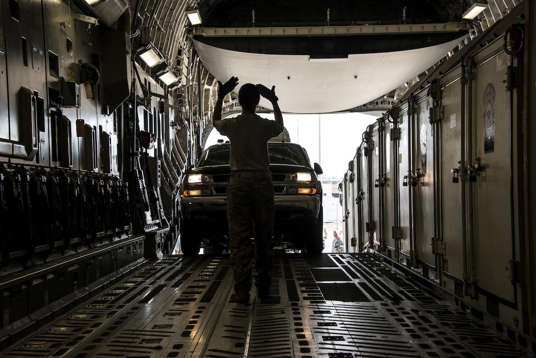 A member of the Air Force makes hand signals as a vehicle drives into an aircraft.
