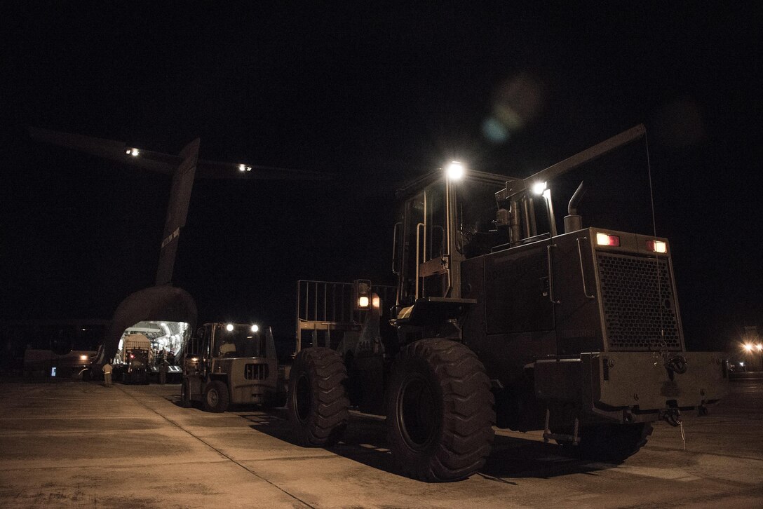 A line of machinery waits to unload supplies and equipment from an aircraft.