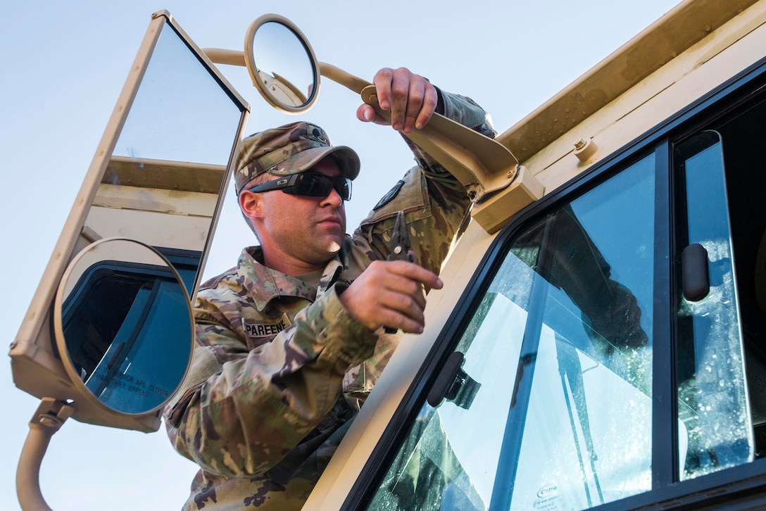 A soldier adjusts a mirror on the outside of a military vehicle.