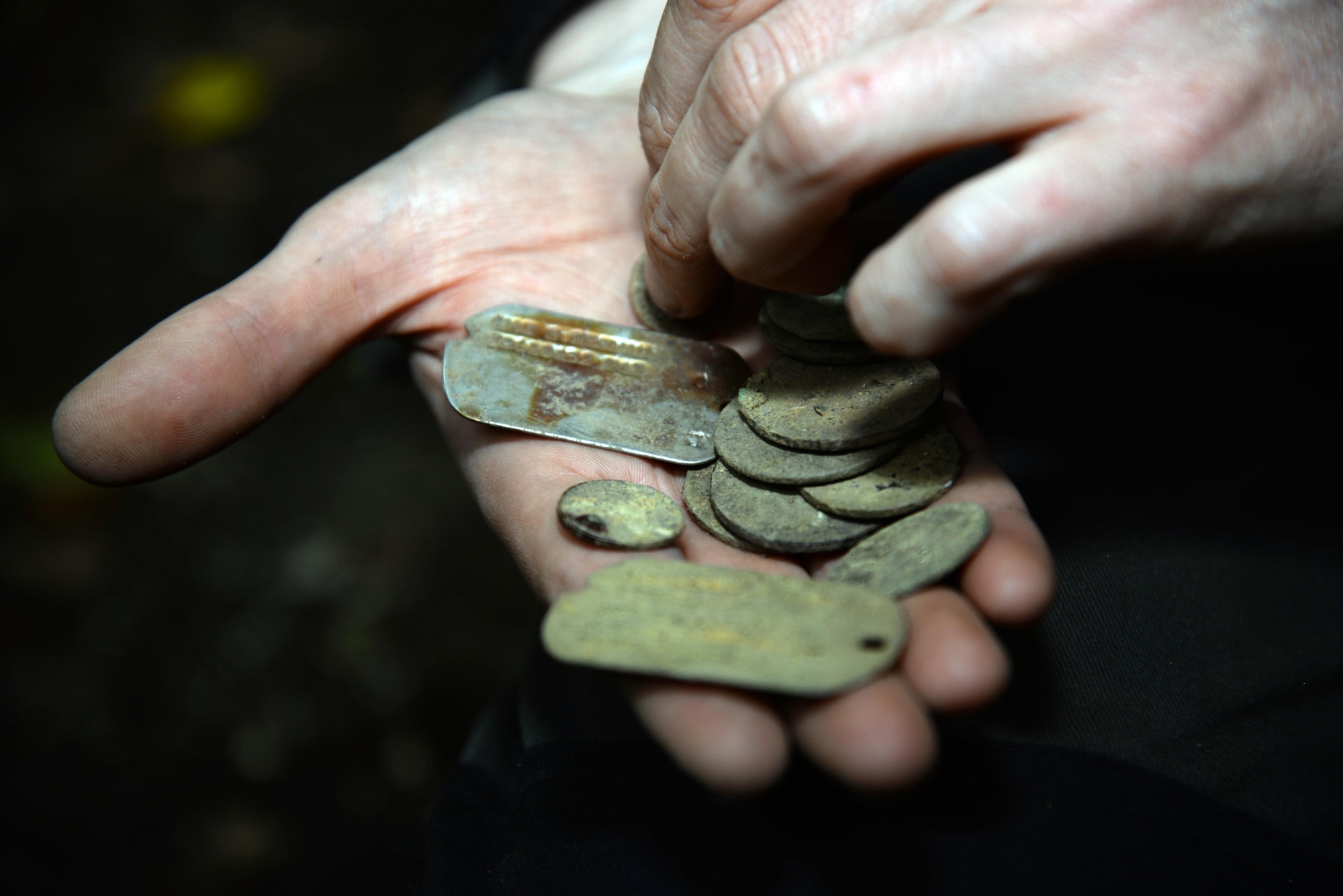 A volunteer hold dog tags and coins recovered from archeological dig