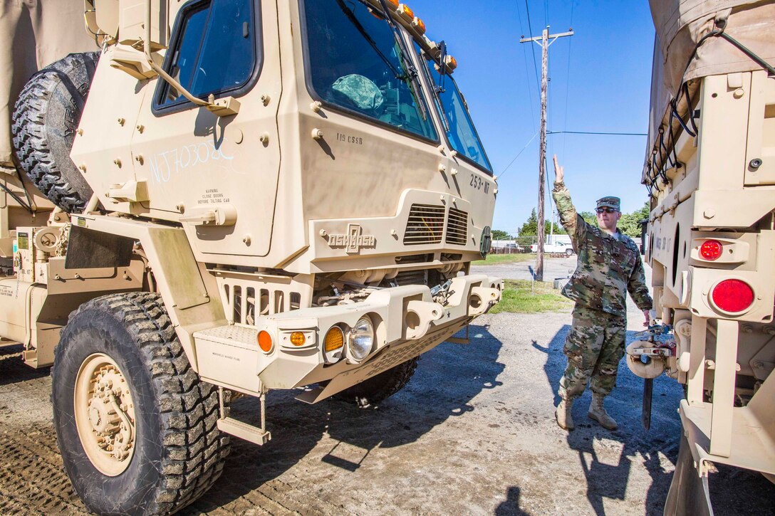 A soldier gives hand signals to guide a light medium tactical vehicle.
