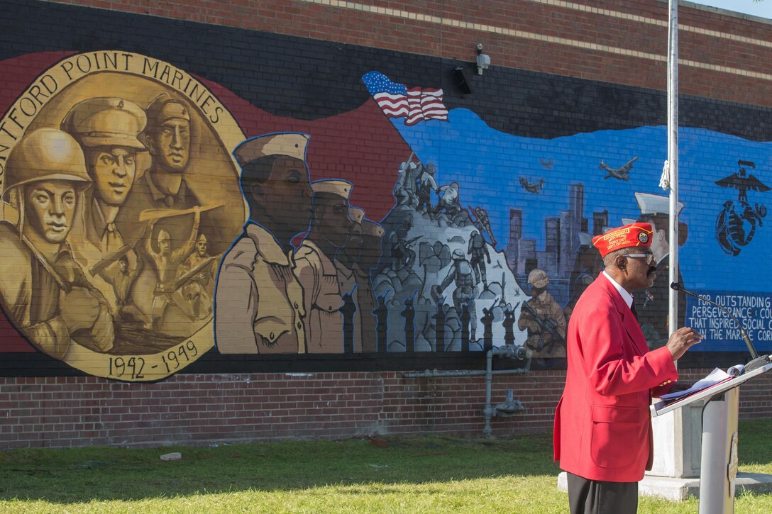 A man speaks at a podium in front of a mural.