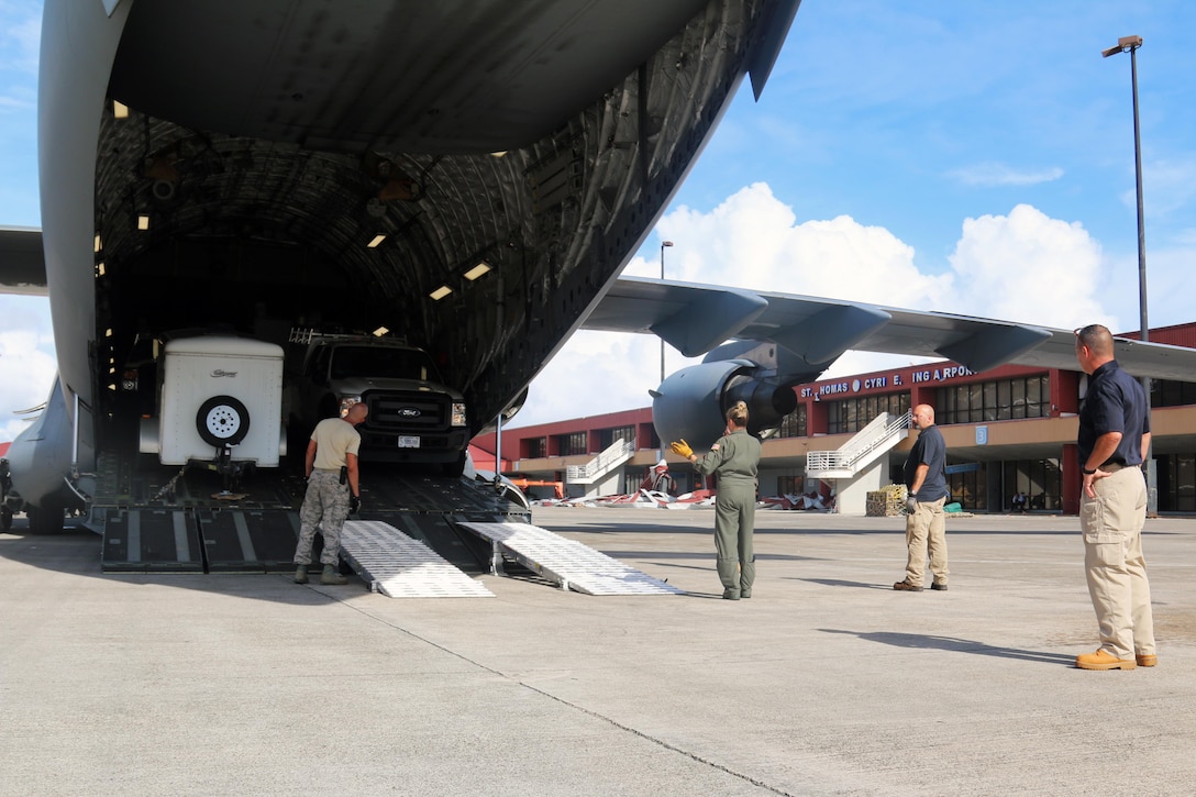 Airmen stand behind an aircraft loaded with equipment.