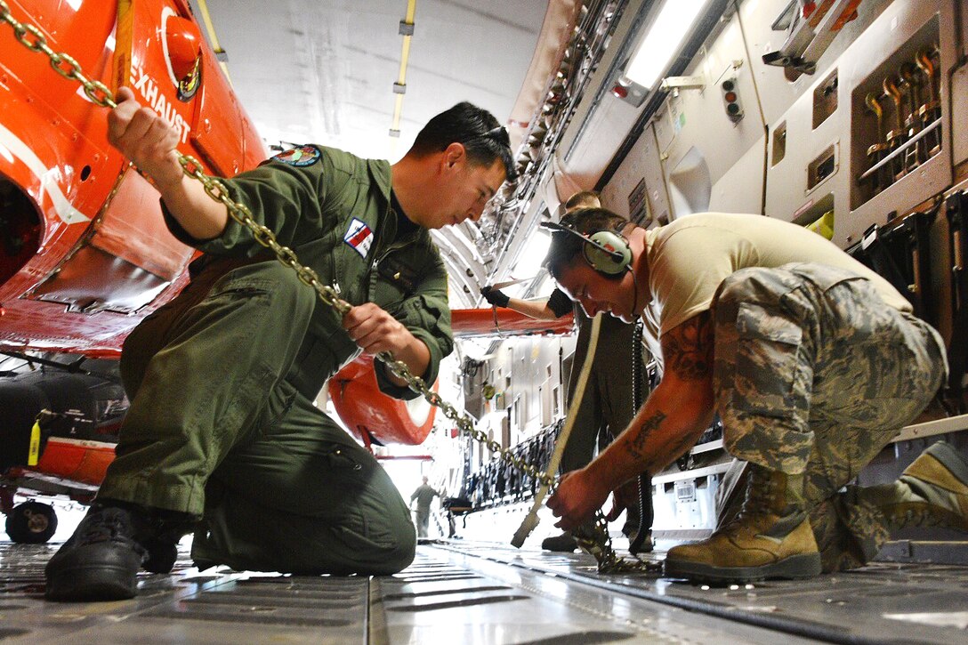 Coast Guard and Air National Guardsmen tighten chains to secure two Coast Guard MH-65 Dolphin helicopters onto a C-17 Globemaster III aircraft