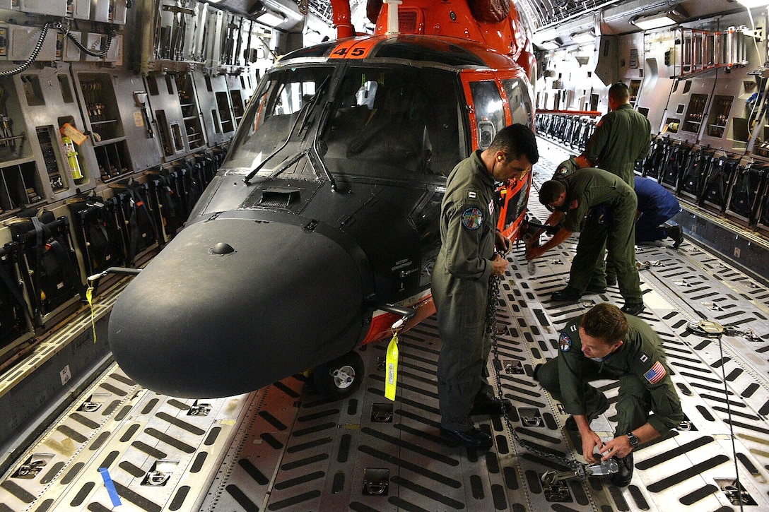 Coast Guard and Air National Guardsmen tighten chains to secure two Coast Guard MH-65 Dolphin helicopters into a C-17 Globemaster III