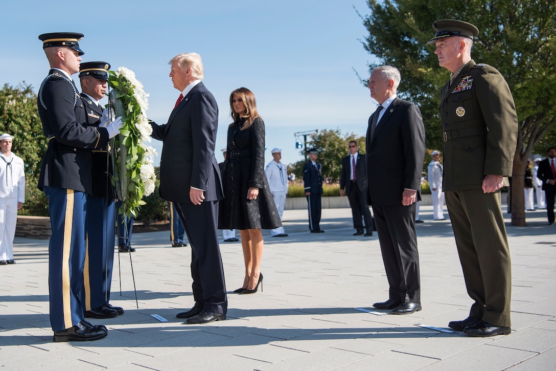 President Donald J. Trump stands in front or a wreath with his wife beside him and Defense Secretary Jim Mattis and Marine Corps Gen. Joe Dunford behind them.