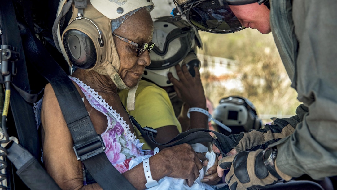 A Marine straps a woman into a helicopter seat.