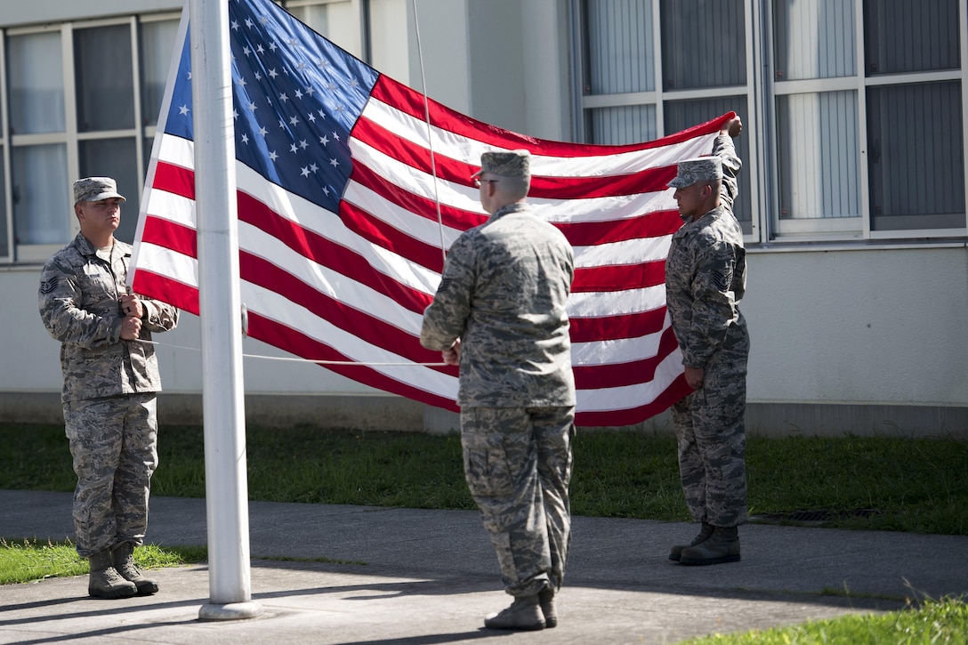 A group of airmen unfurl and raise the U.S. flag during a 9/11 remembrance ceremony