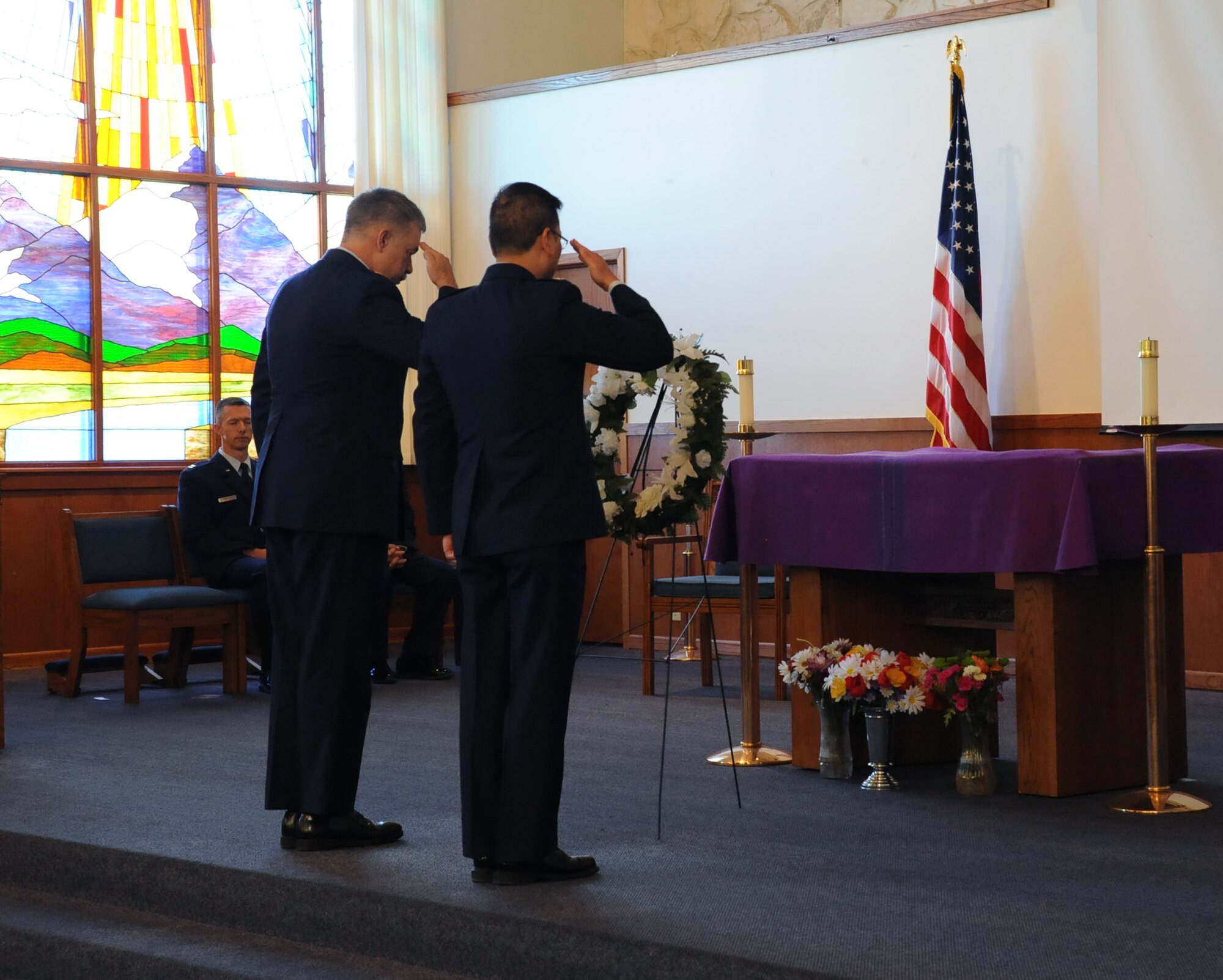 Chaplains (Maj.) Joseph Fisher and (Capt.) Charles Kim, 341st Missile Wing, salute after placing a wreath of flowers on an easel as a tribute to those affected by the 9/11 attacks. Members of Malmstrom Air Force Base, Mont., came together Sept, 11, 2017, at the base chapel to remember those who lost their lives during the Sept. 11, 2001, attacks. (U.S. Air Force photo/Christy Mason)