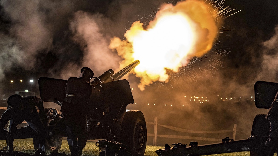 Soldiers fire a cannon into the night sky.