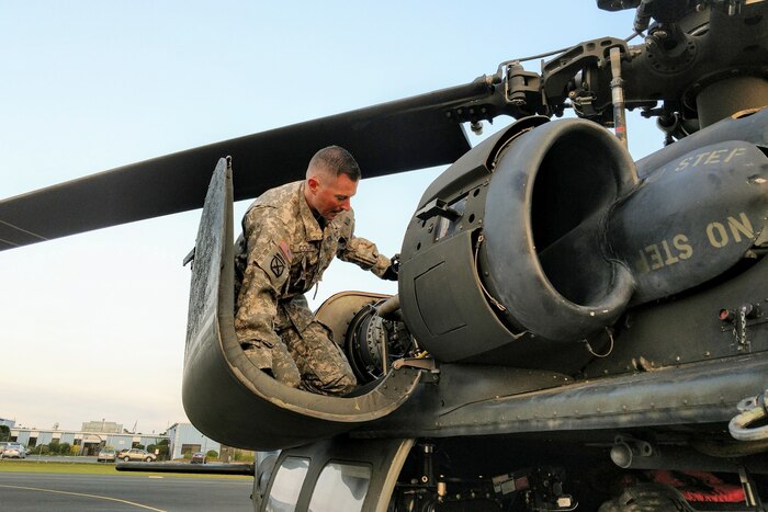 A solider kneels inspecting a helicopter.