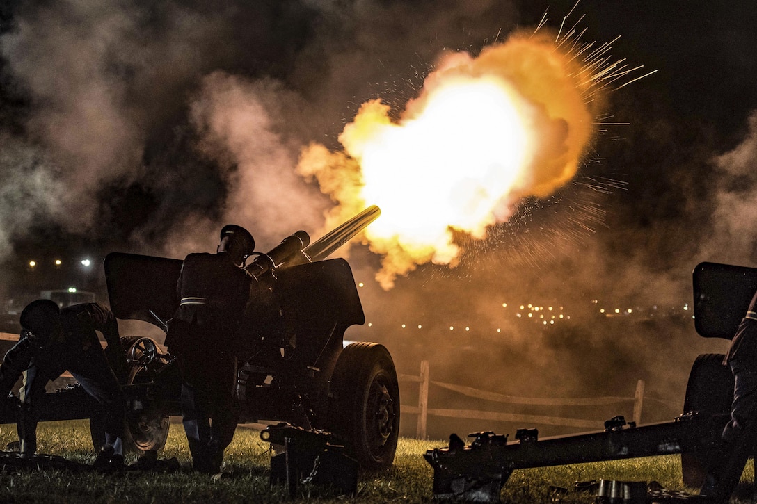 Soldiers fire a cannon into the night sky.