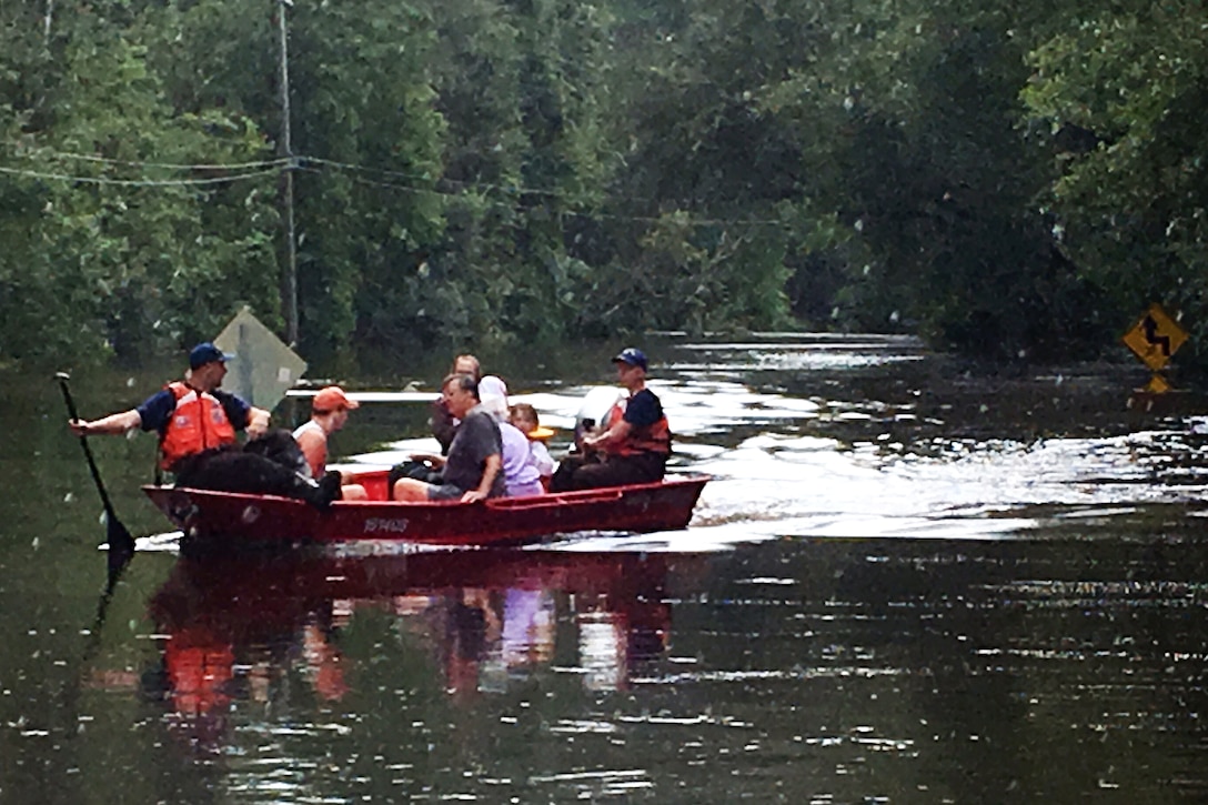 Members of the Coast Guard and civilians ride in a boat past a street sign.