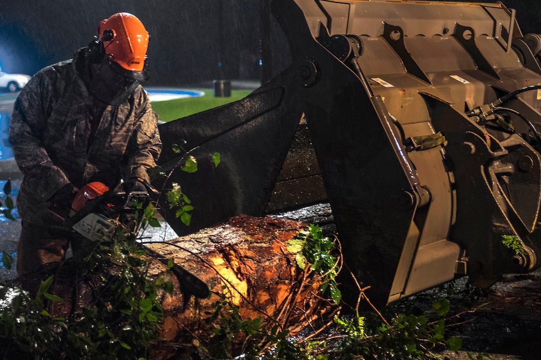 A member of the Air Force uses a chain saw to cut a tree trunk.