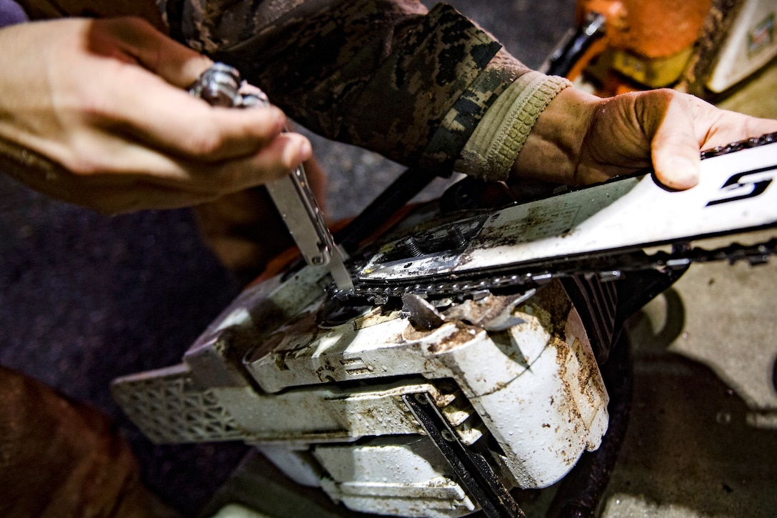 An airman uses a tool to fix a chainsaw.
