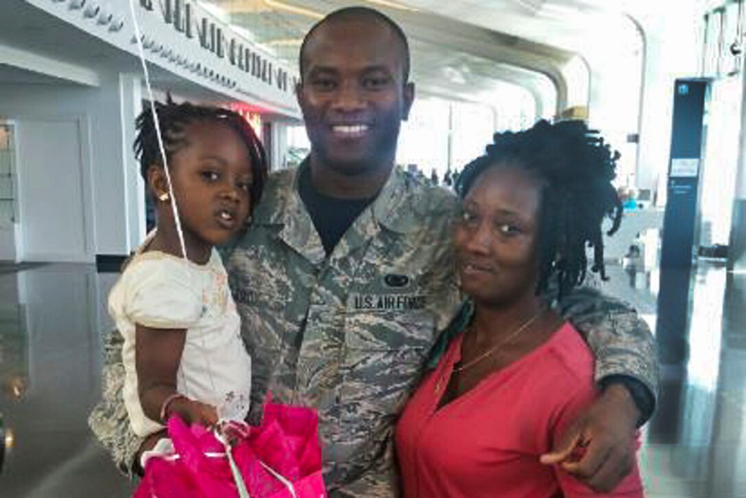 An airman, his wife and daughter pose for a photo at an airport.