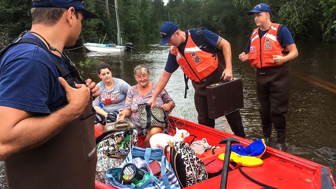 Coast Guardsmen help women load their possessions into a boat.