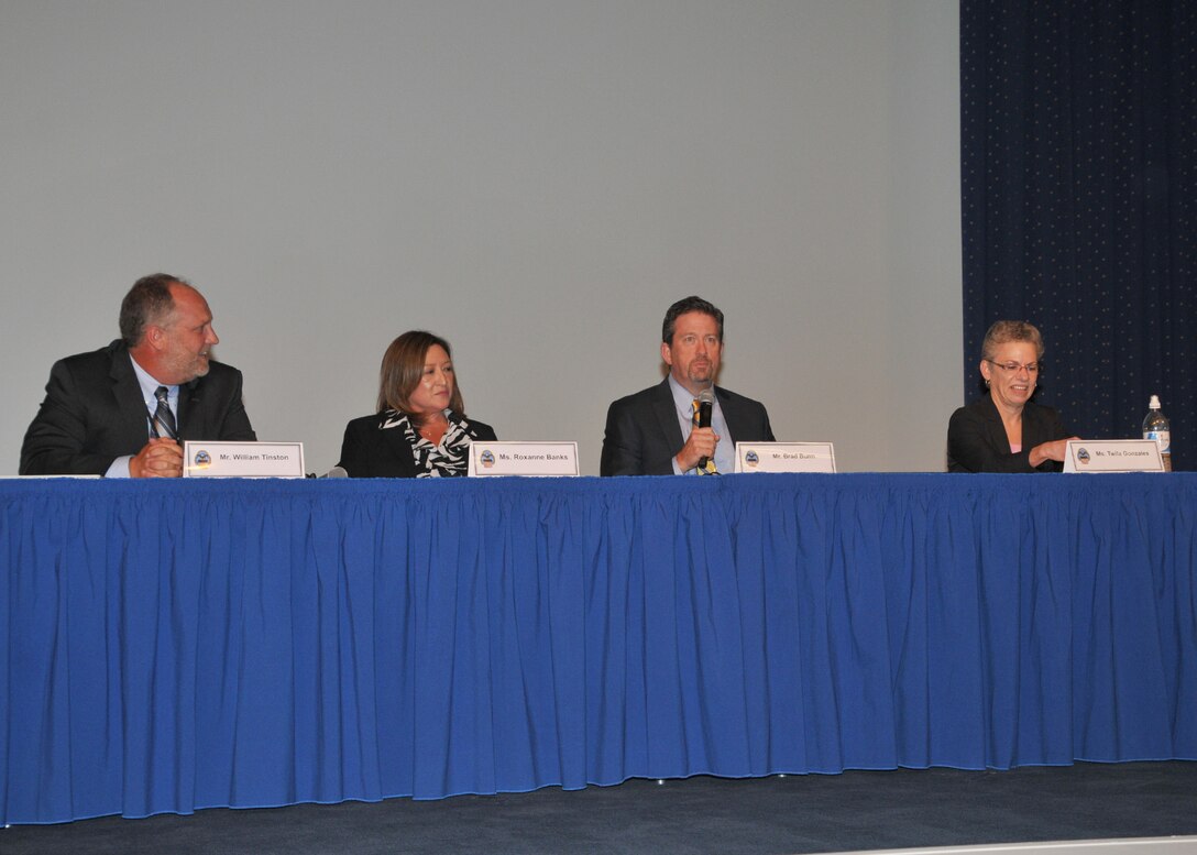 Panel, facing viewer, seated at table in business attire.