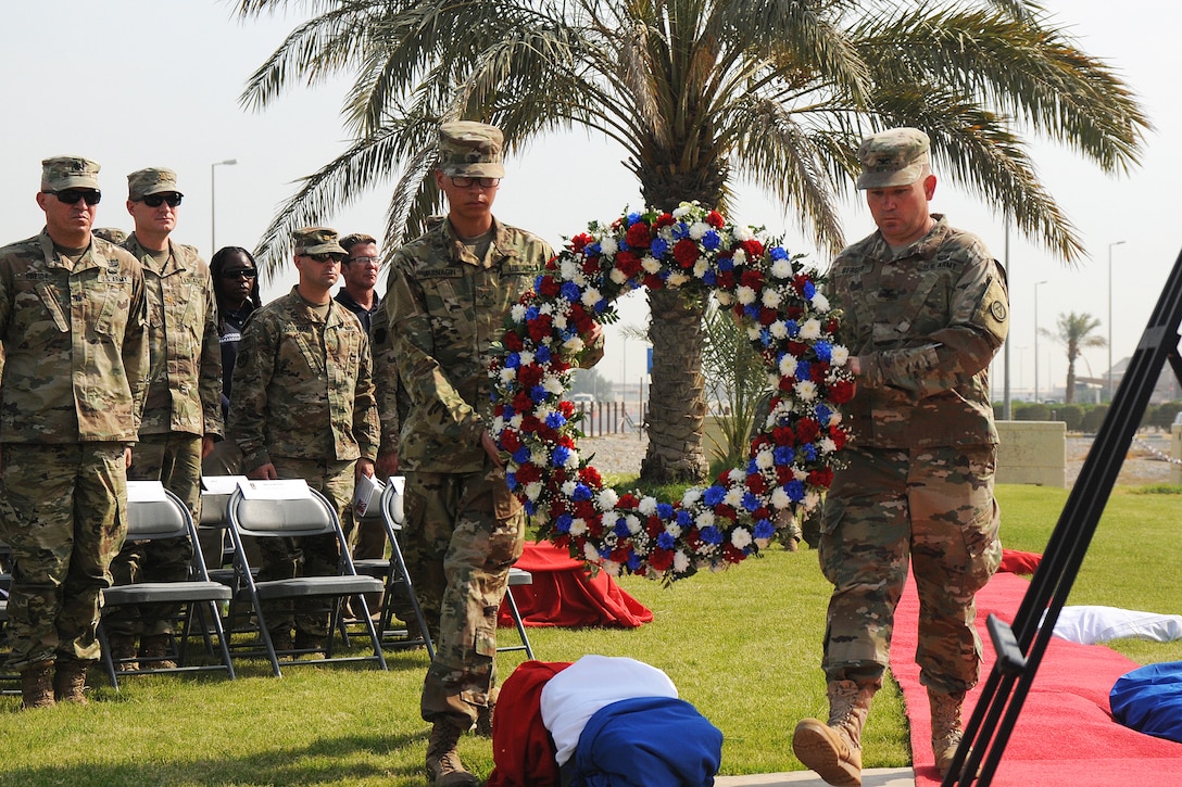 Two soldiers carry a wreath with a group of soldiers standing in the background.