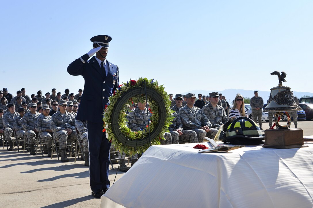 An airman salutes a wreath with service member seated behind him.