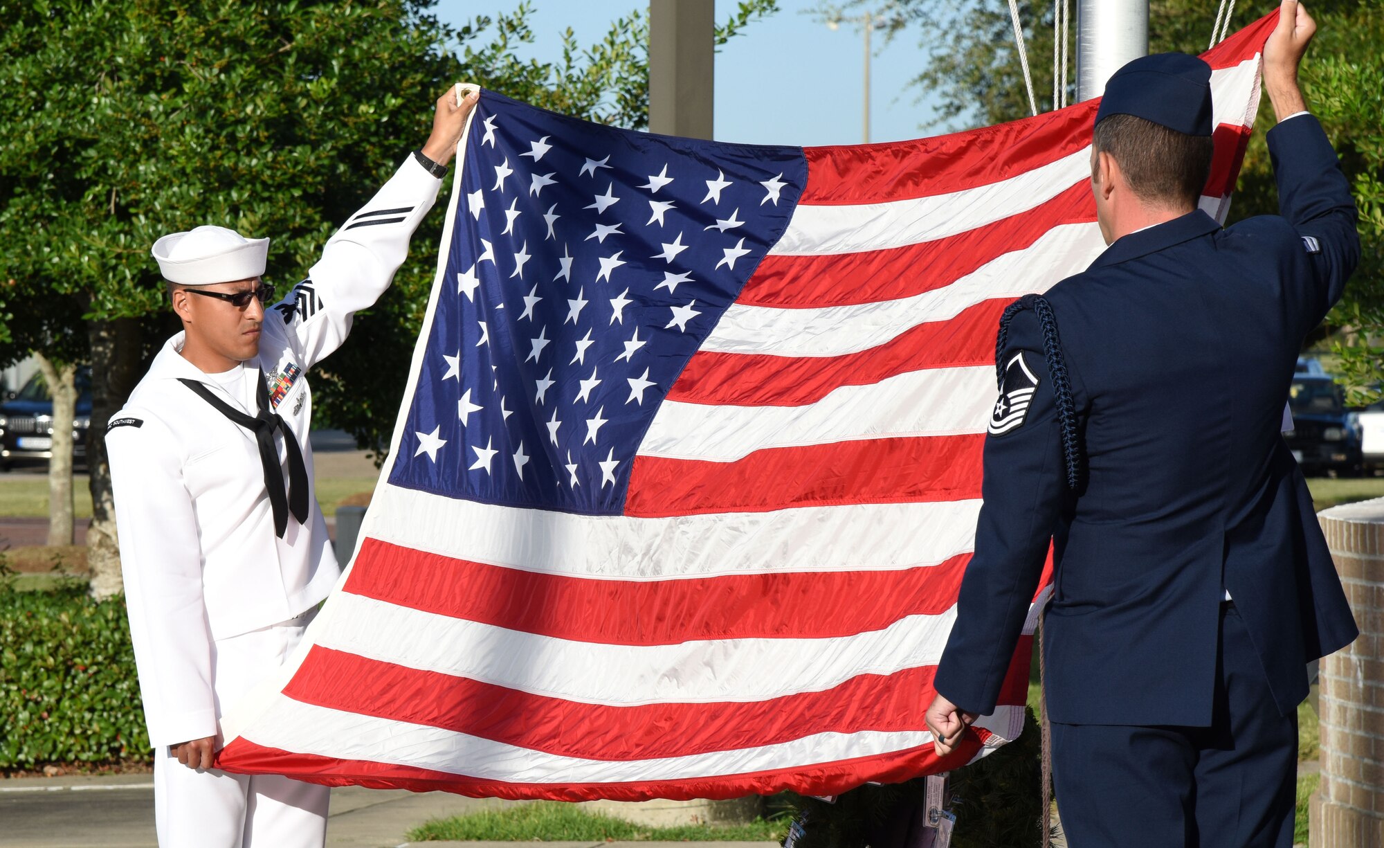 U. S. Navy Aviation Electronics Technician 1st Class Hugo Paez, Center for Naval Aviation Technical Training Unit Keesler student, and Master Sgt. Joshua Anderson, 81st Training Support Squadron Military Training Leader School instructor supervisor, display the U.S. flag during a 9/11 memorial ceremony hosted by the CNATTU Keesler in front of Alho Manor Sept. 11, 2017, on Keesler Air Force Base, Mississippi. The event honored those who lost their lives during the 9/11 attacks. (U.S. Air Force photo by Kemberly Groue)