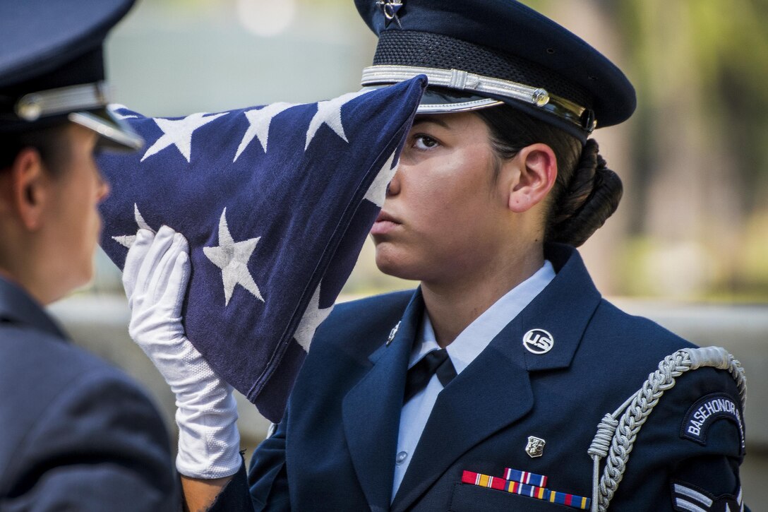 An airman with a white glove holds a folded flag at eye level.