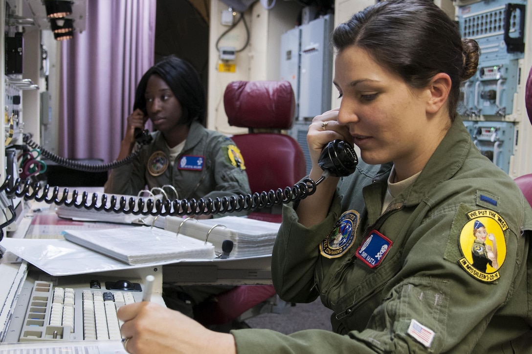 Two airmen talk on phones at a control panel.