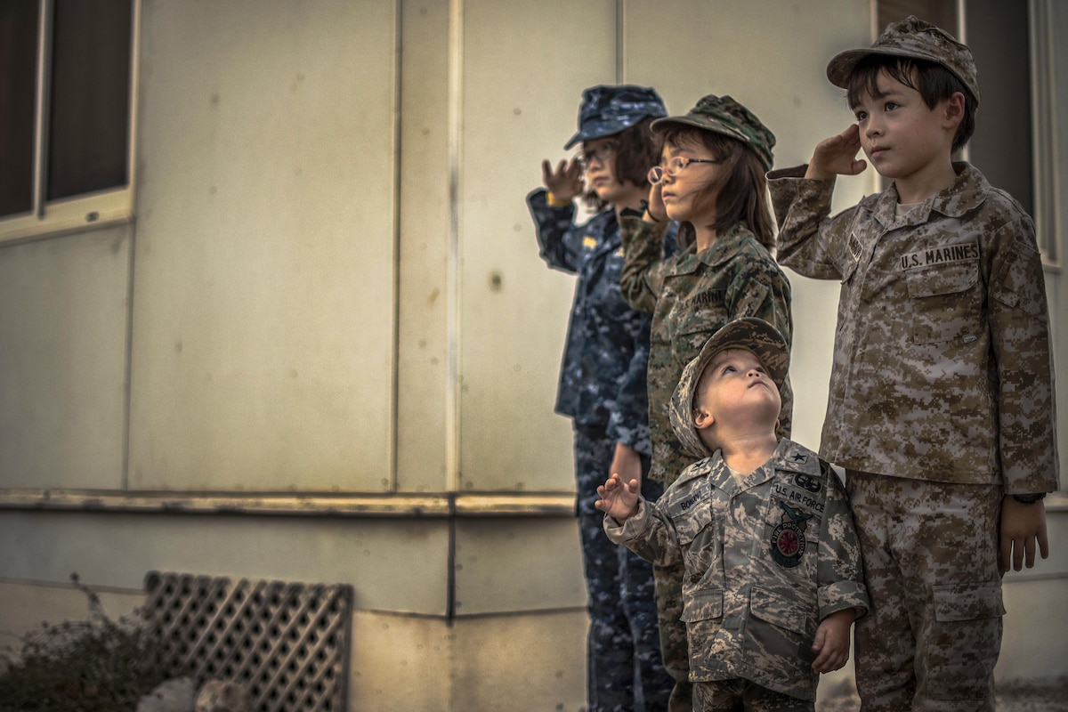 Four children in military uniforms stand and salute during a ceremony.