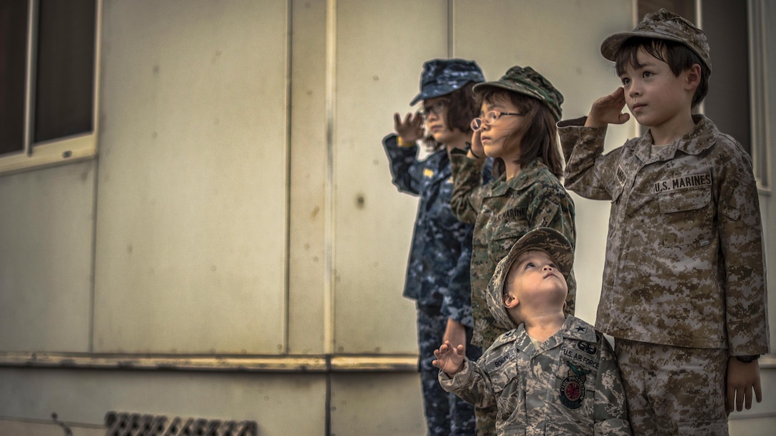 Four children in military uniforms participate in a ceremony.