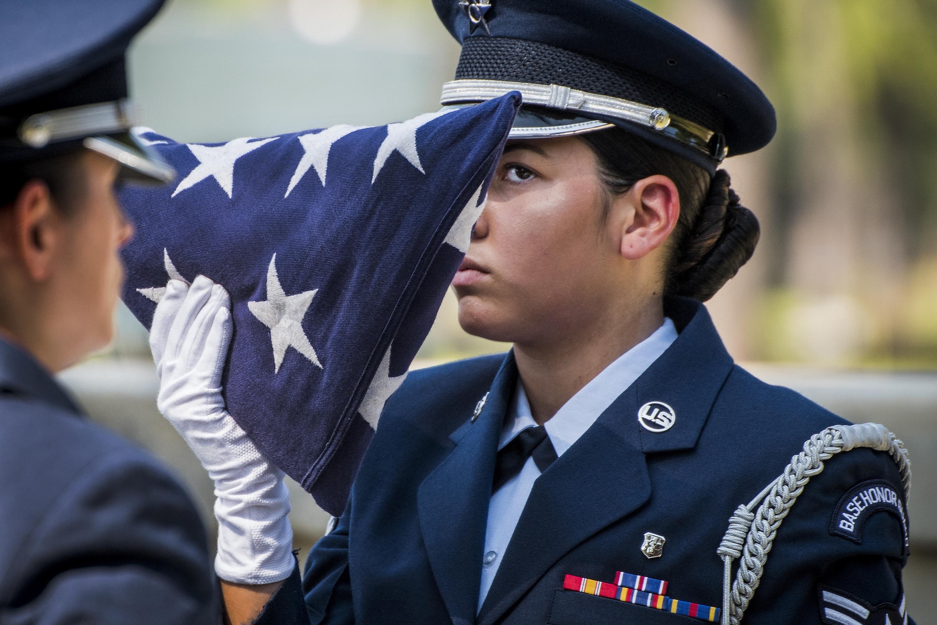 An airman with a white glove holds a folded flag at eye level.