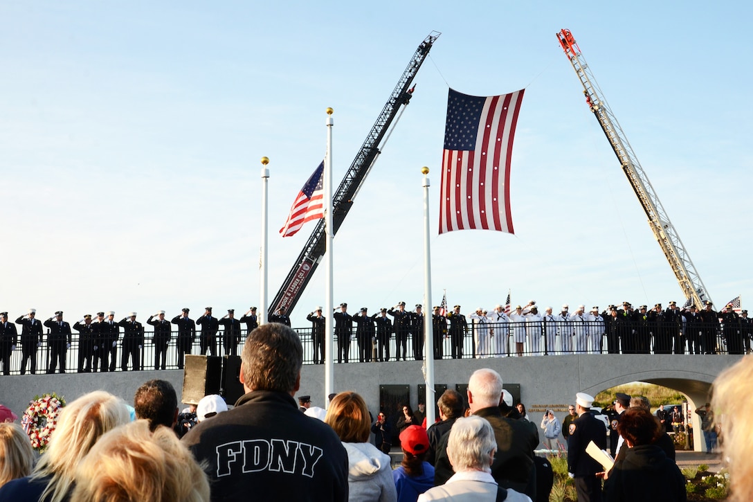 Sailors and members of the New York Fire Department members salute the American flag as it is lowered to half-staff