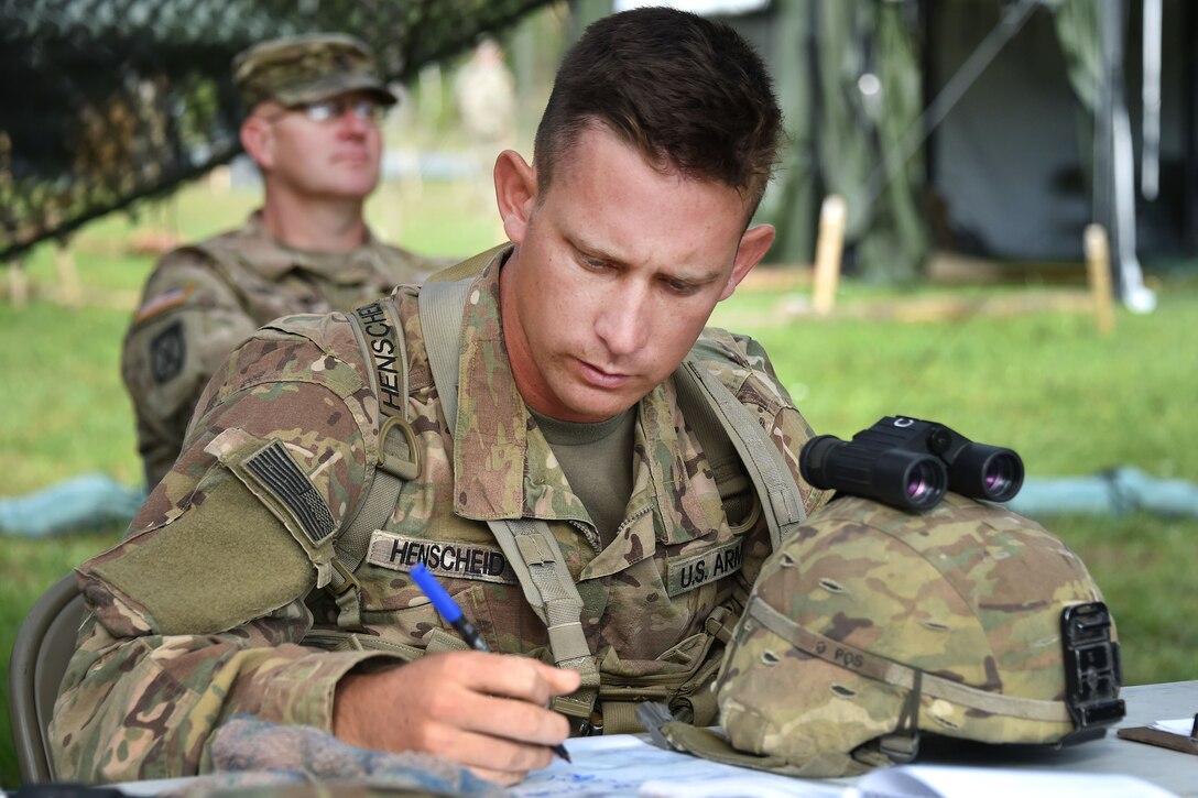 A soldier reads a map while seated at a table.
