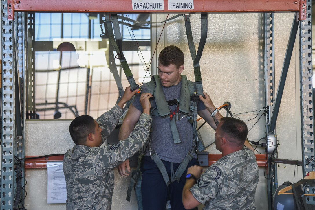 Staff Sgt. Robert Rodriguez, 1st Operation Support Squadron Aircrew Flight Equipment specialist, and U.S. Staff Sgt. James Long, 1st OSS Survival, Evasion, Resistance and Escape specialist, secure Paul Felder, Ultimate Fighting Championship lightweight division fighter, into a parachute simulator at Joint Base Langley-Eustis, Va., Sep. 8, 2017.