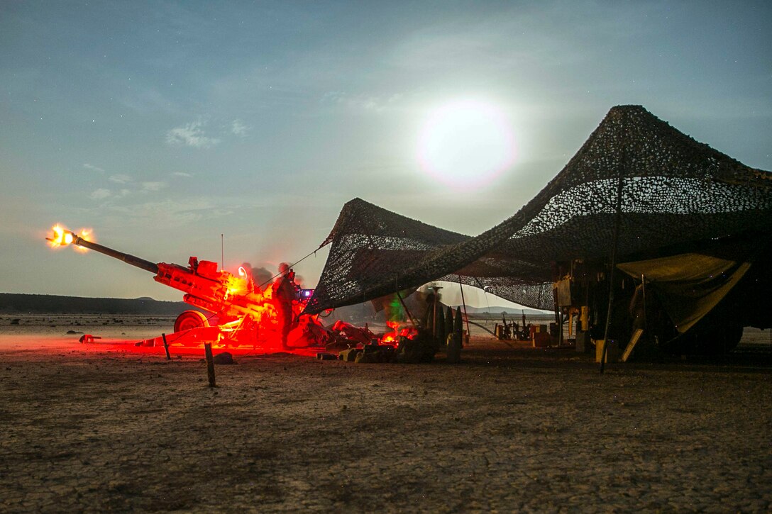 Marines stand by a howitzer as it fires adjacent to a tent.