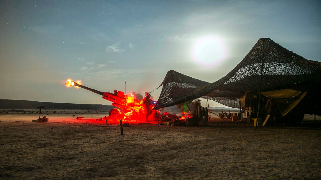 Marines stand by a howitzer as it fires adjacent to a tent.