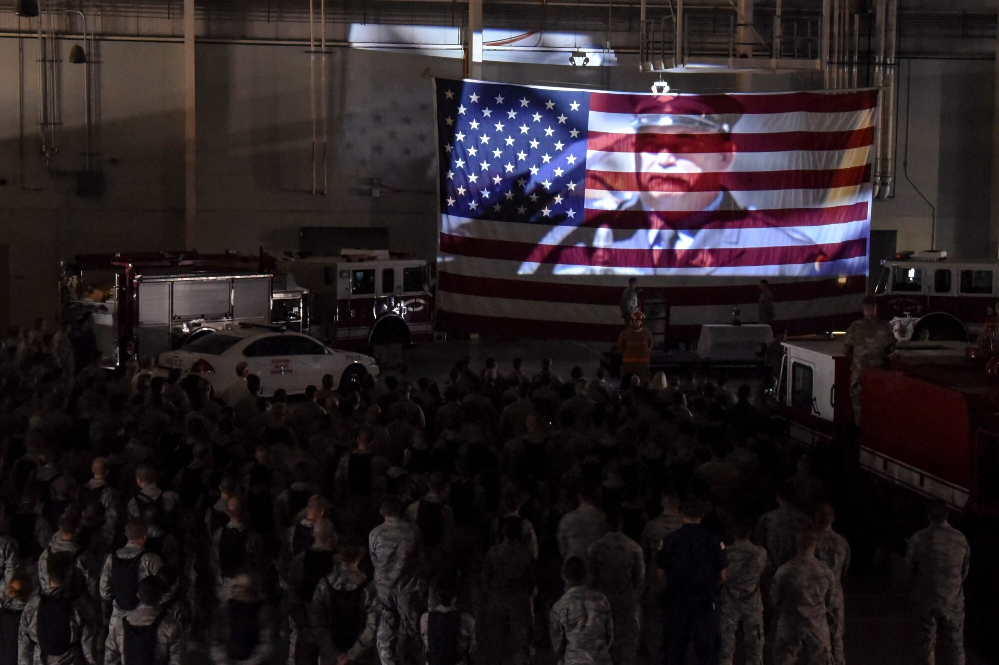 Attendees of the 9/11 Memorial watch a tribute video projected onto a flag at the  Louis F. Garland Department of Defense Fire Academy high bay on Goodfellow Air Force Base, Texas, Sept. 11, 2017. The video showed footage of the towers falling and paid tribute to all the first responders who died on 9/11. (U.S. Air Force photo by Airman Zachary Chapman/Released)