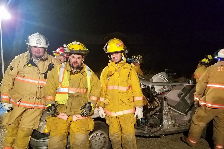 Sean Baker, middle, volunteer firefighter and aircrew flight equipment mechanic for M1 support services at the 40th Helicopter Squadron, poses for a photo after extraction training Mar. 21, 2017, at the Sand Coulee Volunteer Fire Department, Mont.