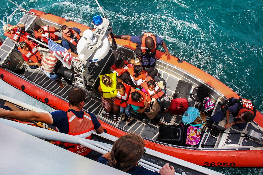 A small boat filled with people sits next to a cutter in the water.