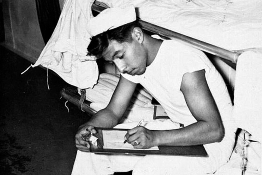 A sailor leans over a clipboard and writes on paper.