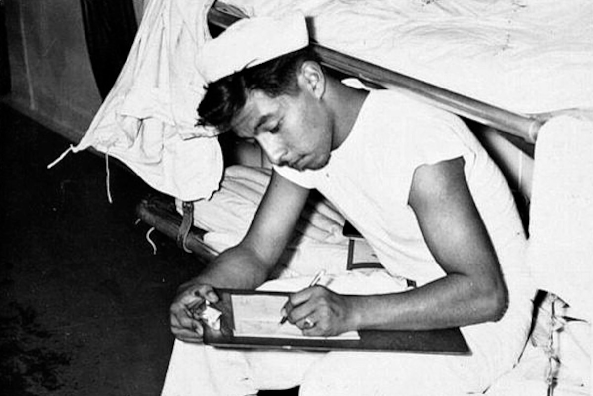 A sailor leans over a clipboard and writes on paper.