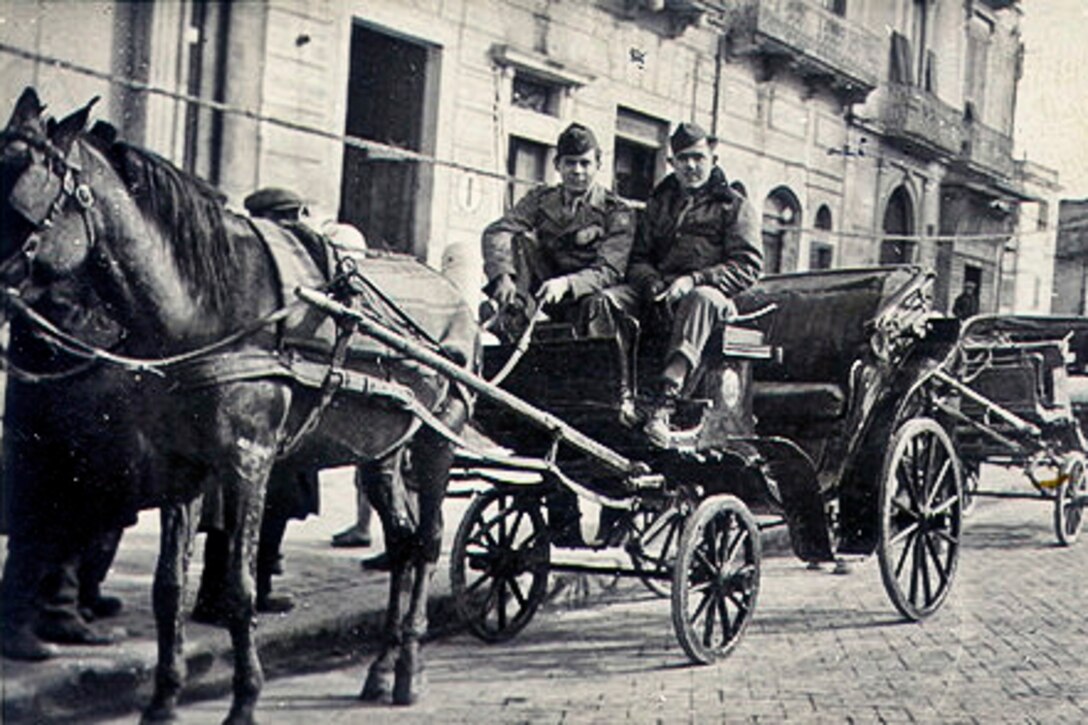 Two service members sit in a carriage pulled by a horse.