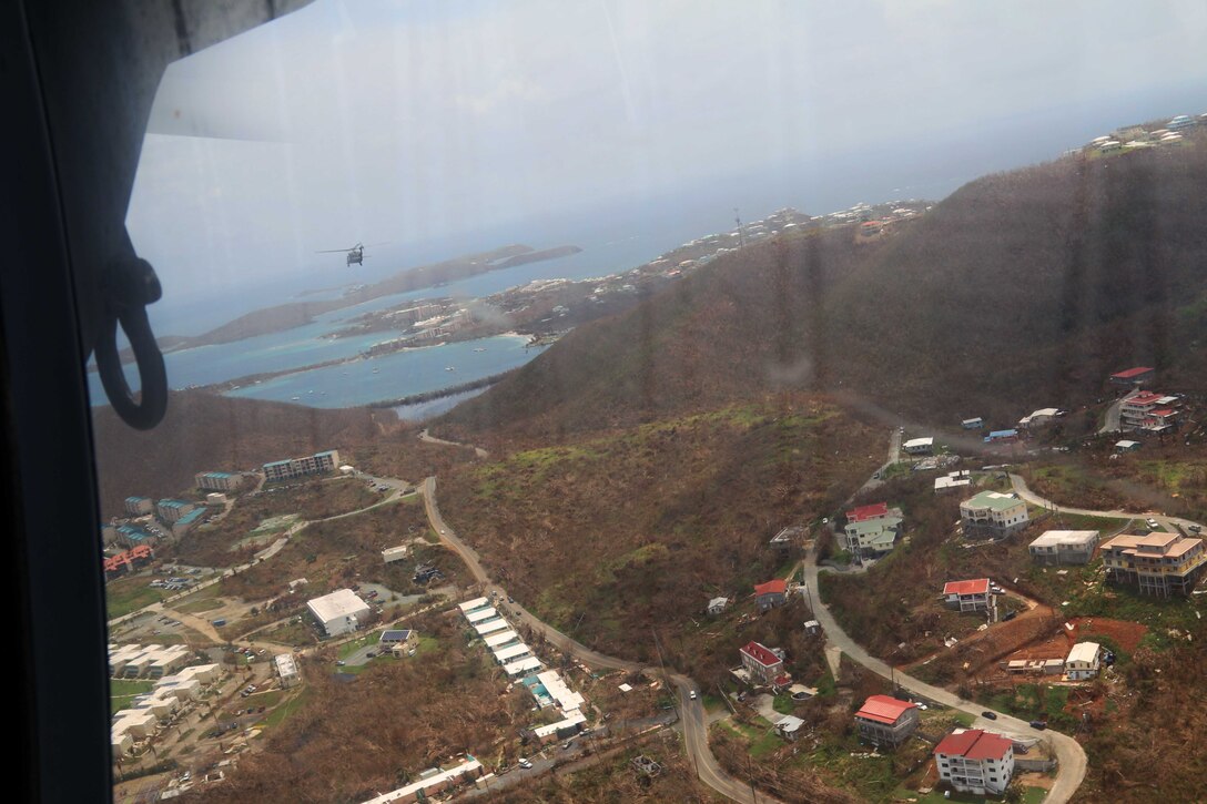 As seen through the window of an aircraft, a helicopter flies over land, water and buildings.
