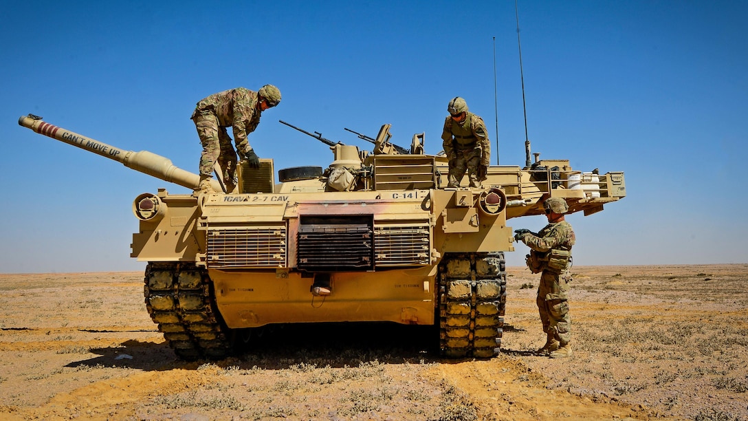 Three soldiers stand on or near a tank while inspecting it.