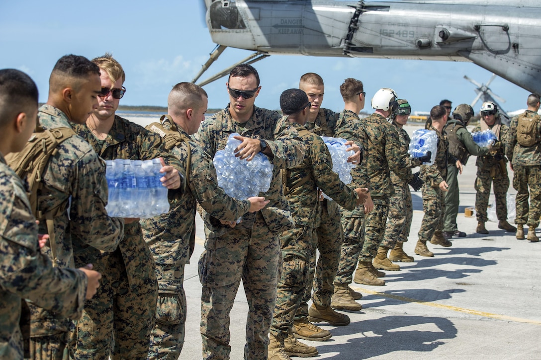 Marines stand in a line passing bottles of water out of an aircraft.