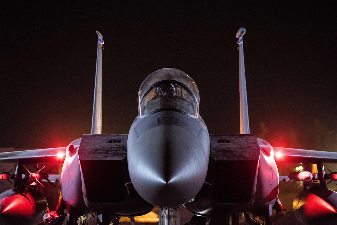 An airman works in the cockpit of an aircraft on a dark flightline.