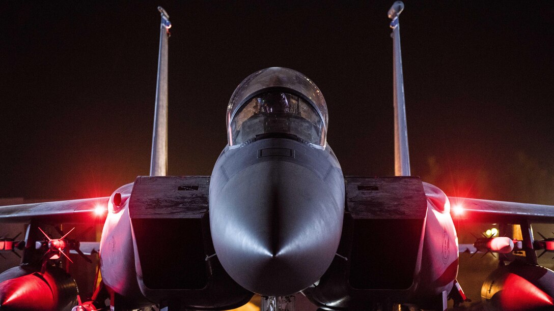 An airman works in the cockpit of an aircraft on a dark flightline.