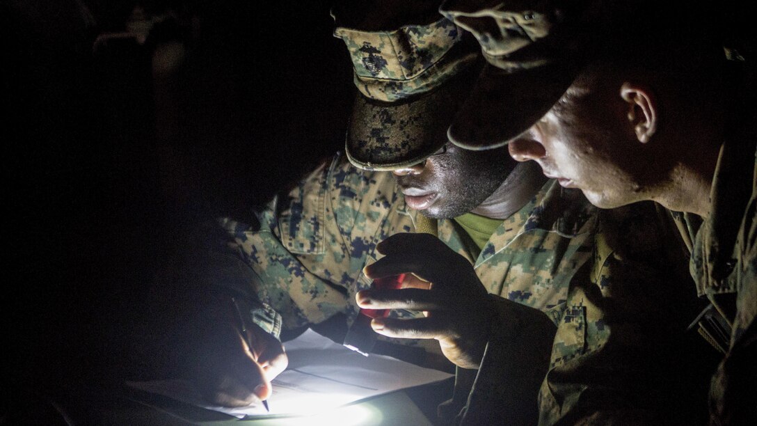 Two Marines look over notes by flashlight.